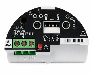 Back view of a round black electronic module with a green two-terminal block (plus/ground), a red push button, and a white connector area for wiring.